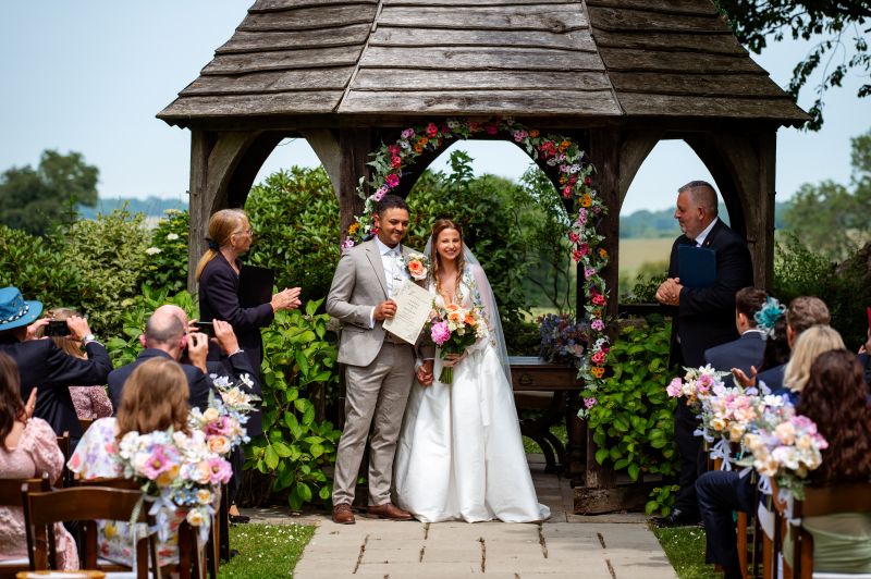 A couple stand with their wedding certificate after getting married in Godric's Garden, Outdoor licenced ceremony area at Solton Manor, near Whitstable, Kent, England