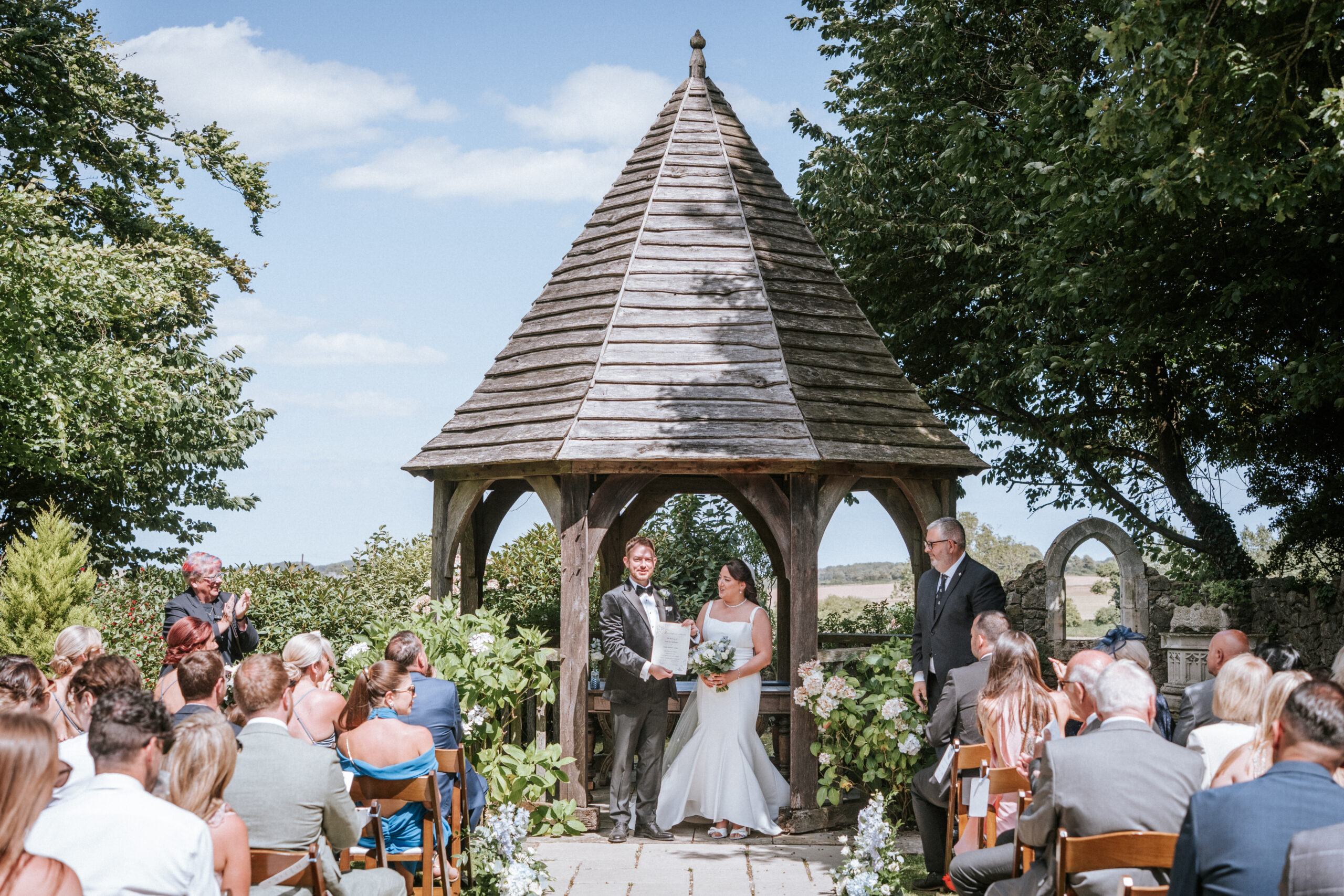 A couple say I do under the oak gazebo in the outdoor ceremony space, Godric's Garden, at Solton Manor, near Canterbury, Kent, England, United Kingdom