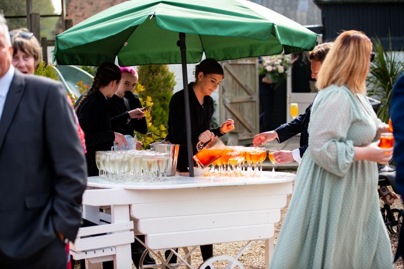 a member of the front of house team at solton manor serve aperol during a drinks reception on the lawn