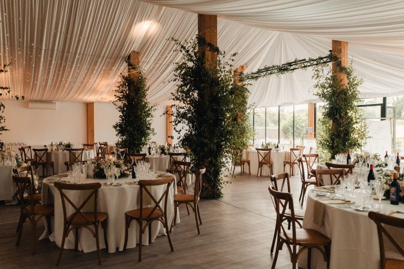 The Dutch Barn, set up with cross back chairs and round tables ready for a reception at Solton Manor, Dover, Kent, England. Column dressings by Chic Wedding and Events